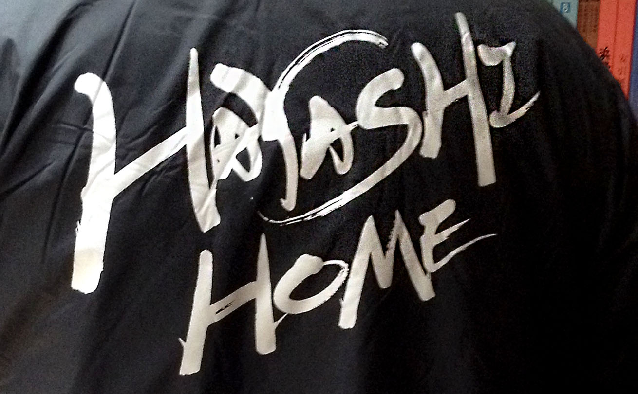 黒いジャケットの背面へシルバーで印字した「HAYASHI HOME」の筆文字ロゴ