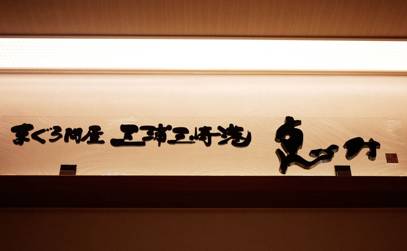 店内上部に設置された横書きの「まぐろ問屋三浦三崎港 恵み」の筆文字看板