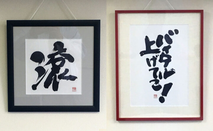 社内の壁に額装された筆文字作品『滾』と『バイタル上げてこ！』