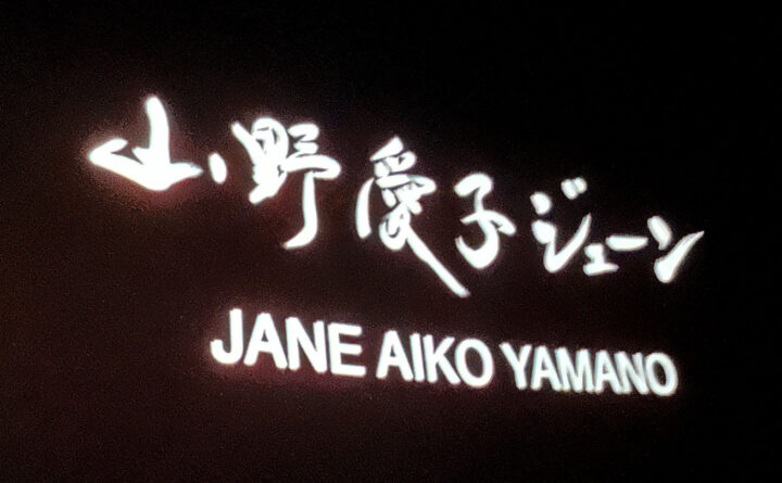 スクリーンに映し出された「山野 愛子 ジェーン」の筆文字
